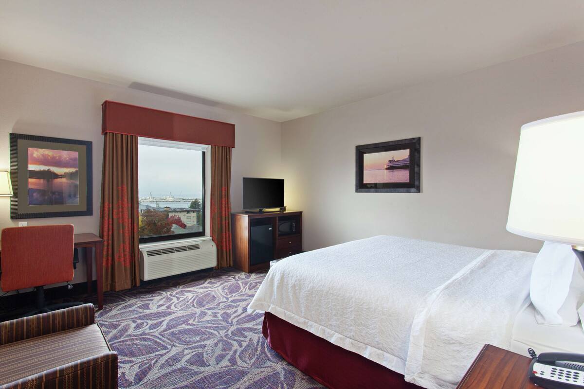 A hotel room with a bed, a desk, a chair, a TV, and a window with curtains.