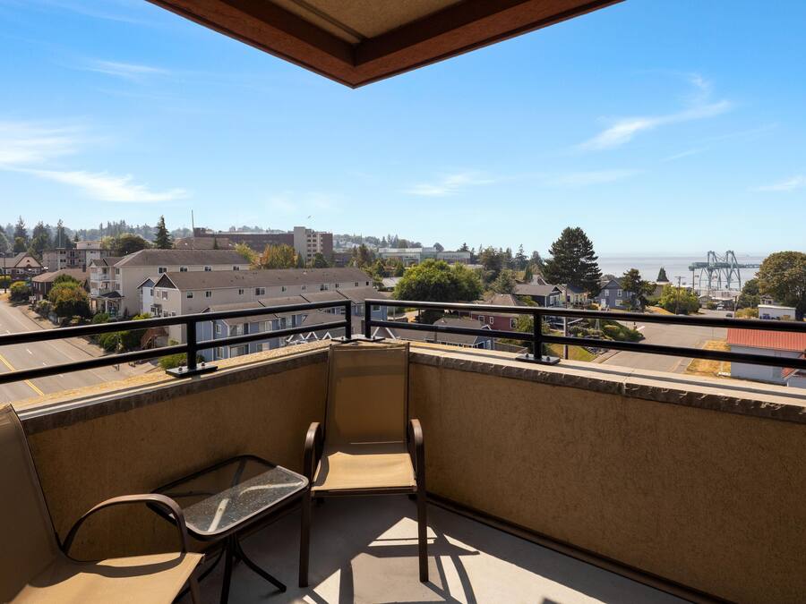 A balcony with a view of a cityscape, a bench, and a railing.