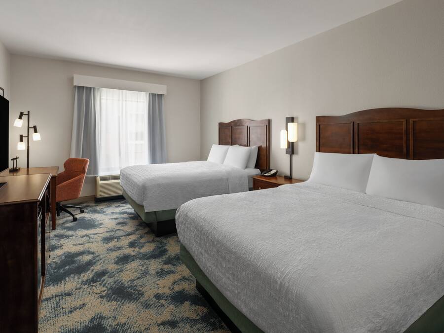 Habitación de hotel con dos camas, un escritorio, una silla, un televisor y una ventana con cortinas.