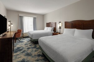 Habitación de hotel con dos camas, un escritorio, una silla, un televisor y una ventana con cortinas.
