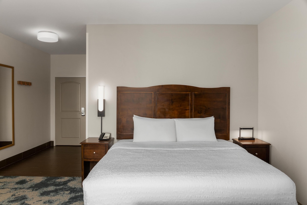 Et hotelværelse med en stor seng, et natbord, en lampe og en dør.