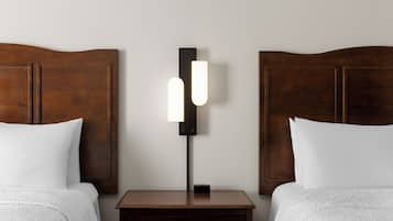 A hotel room with two beds, a nightstand, and a wall-mounted lamp.