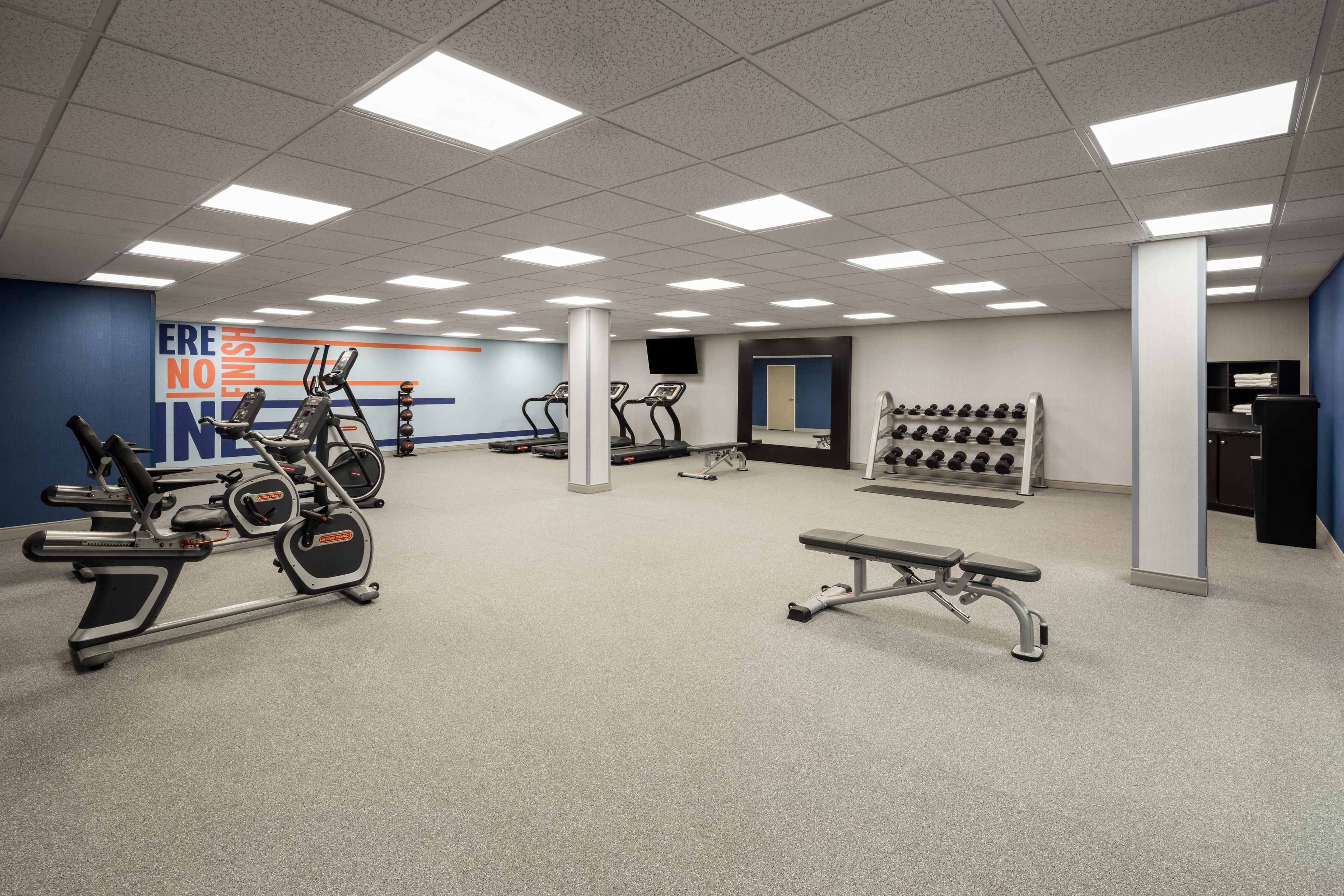 A gym with treadmills, elliptical machines, a bench, and a wall with motivational text.