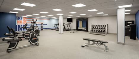 Un gimnasio con cintas de correr, elípticas, una banca y una pared con mensajes motivacionales.