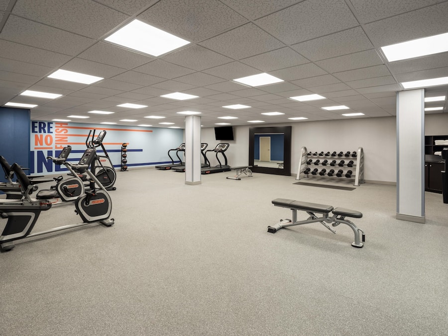 A gym with treadmills, elliptical machines, a bench, and a wall with motivational text.