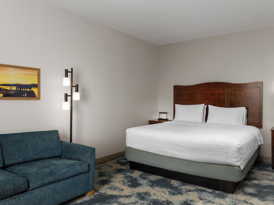 Una camera d'albergo con un letto, un comodino, una lampada, un divano e un quadro appeso al muro.