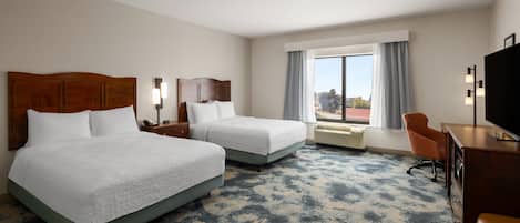 A hotel room with two beds, a desk, a chair, a television, and a window with curtains.