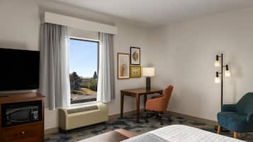 Una camera d'albergo con un letto, una scrivania, una sedia, un televisore e una finestra con tende.