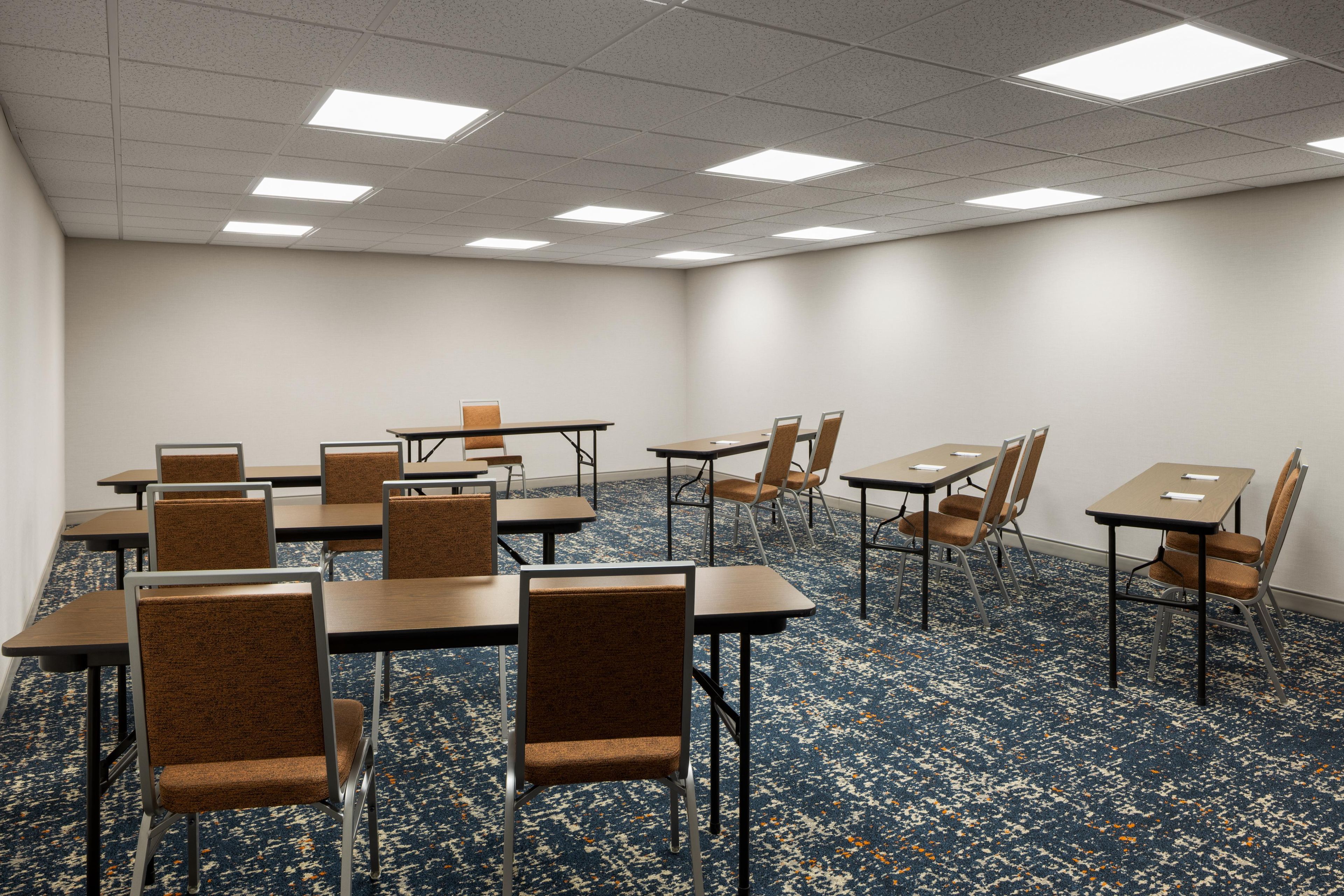 A conference room with tables and chairs, carpeted floor, and ceiling lights.