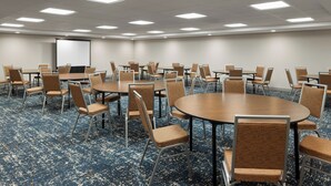 A conference room with multiple tables and chairs, a projector screen, and a carpeted floor. - Hampton Inn Seattle/Everett (Everett)