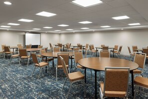 A conference room with multiple tables and chairs, a projector screen, and a carpeted floor. - Hampton Inn Seattle/Everett (Everett)