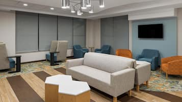 A modern lounge area with a grey sofa, blue and orange chairs, a flat-screen TV, and a patterned carpet.