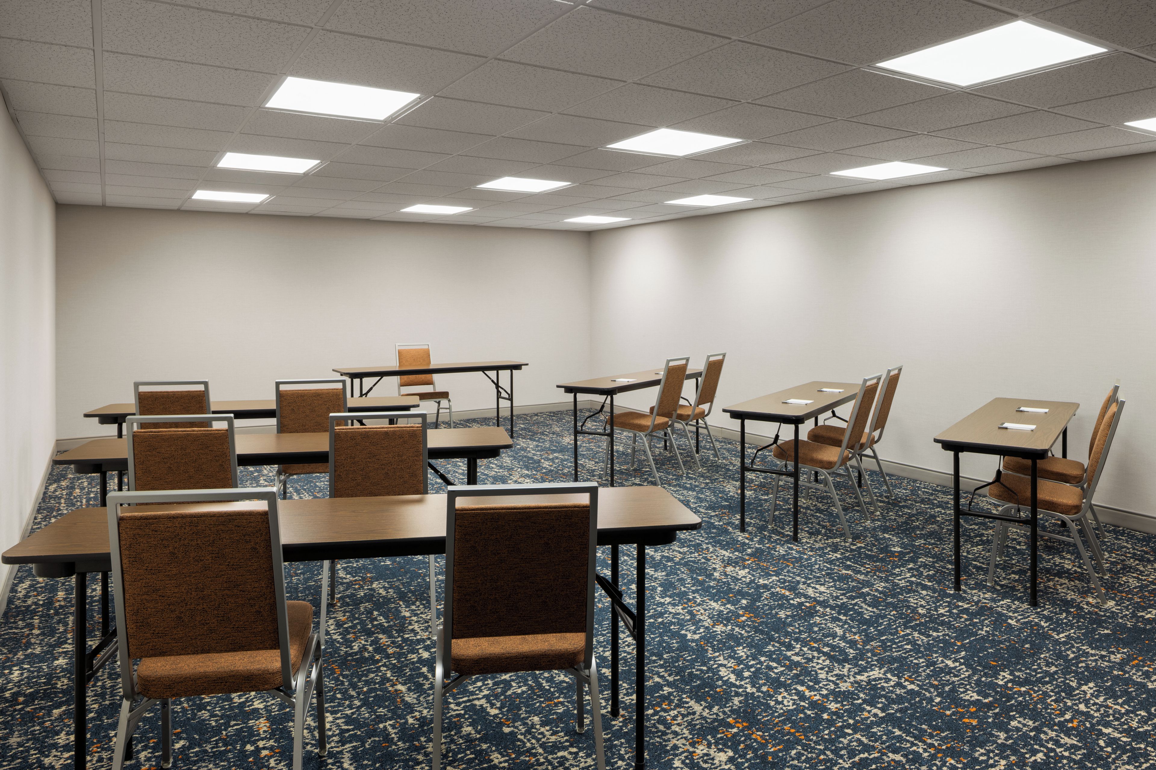 A conference room with tables and chairs, carpeted floor, and ceiling lights.