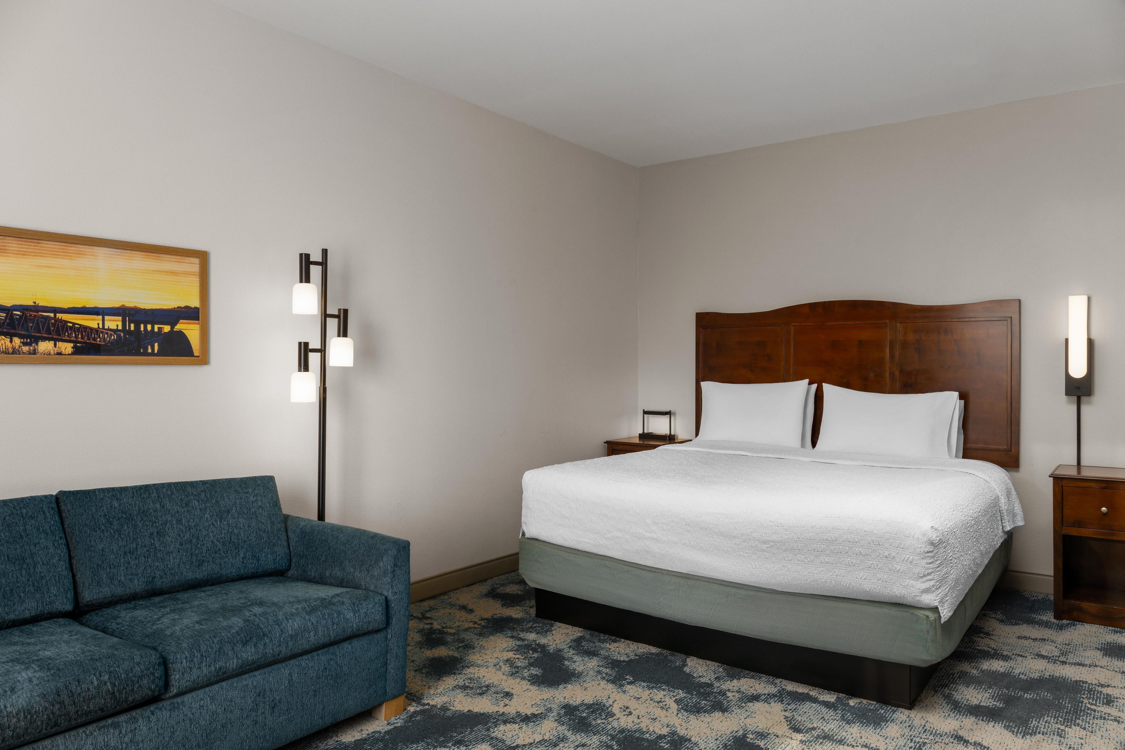 Une chambre d’hôtel avec un lit, une table de chevet, une lampe, un canapé et un tableau au mur.