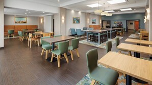A spacious dining area with multiple tables and chairs, a patterned carpet, and ceiling lights. - Hampton Inn Seattle/Everett (Everett)