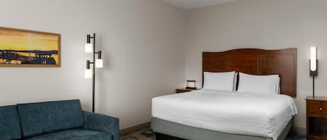 A hotel room with a bed, a nightstand, a lamp, a sofa, and a painting on the wall.