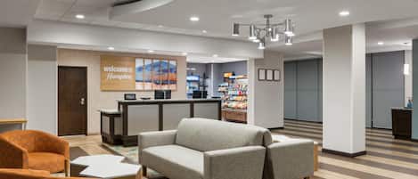 A hotel lobby with a reception desk, seating area, and a wall with a 'Welcome to Hampton' sign.