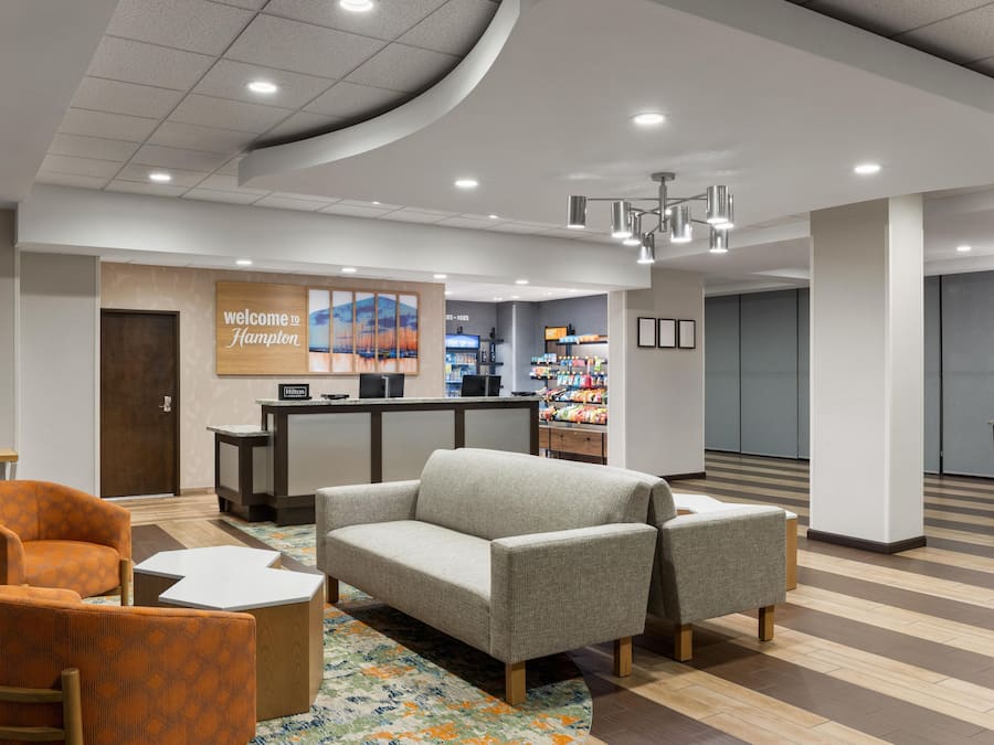 Rebedor d'hotel amb taulell de recepció, zona de seients i paret amb el lema 'Welcome to Hampton'.