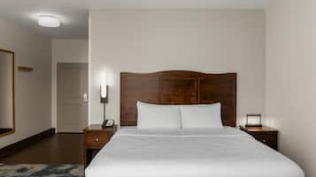 Quarto de hotel com uma cama grande, mesa de cabeceira, abajur e porta.