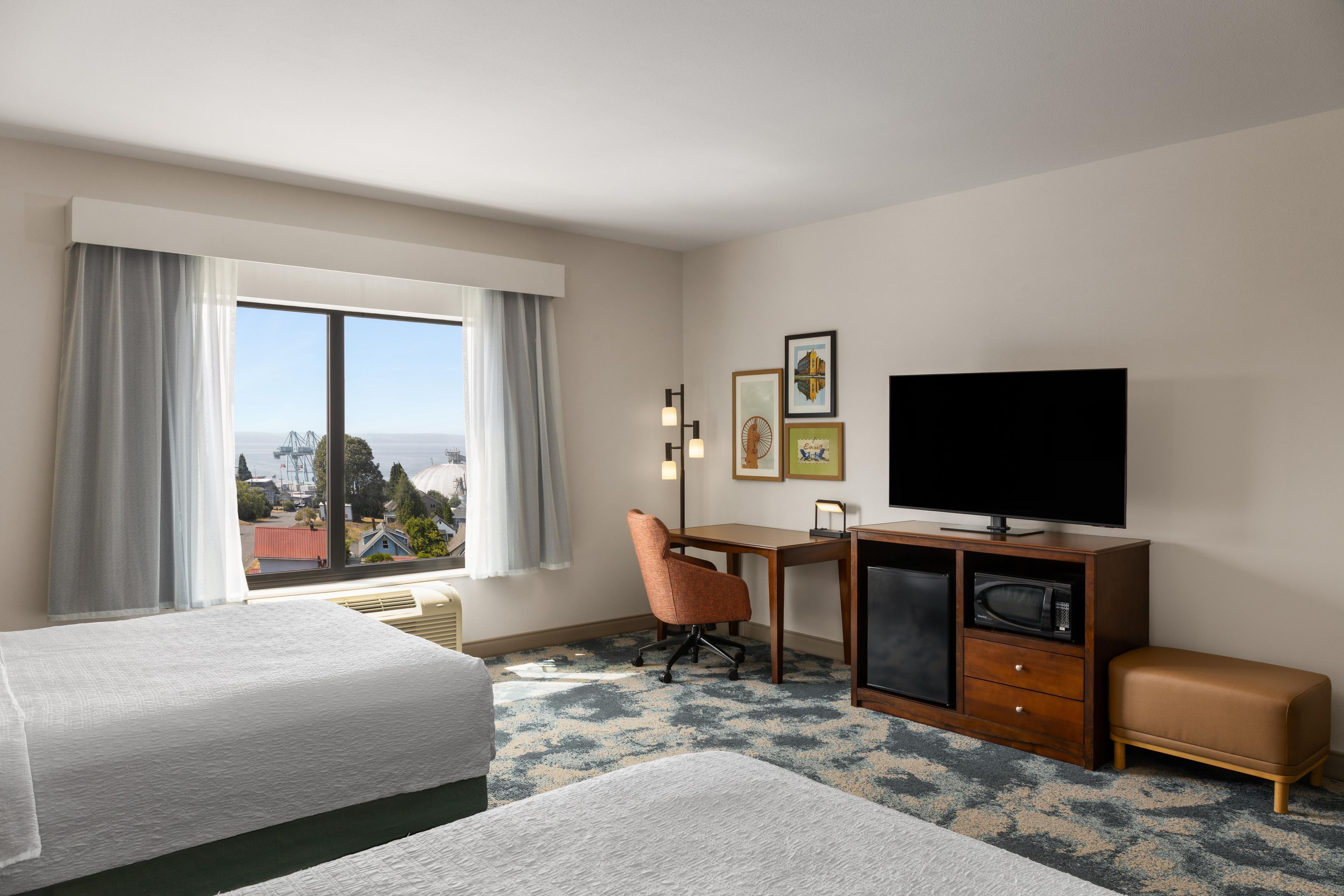Ein Hotelzimmer mit zwei Betten, einem Schreibtisch mit Stuhl, einem Fernseher und Blick auf die Stadt.