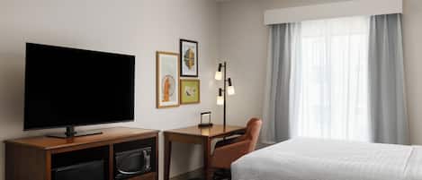 Une chambre d’hôtel équipée d’un téléviseur à écran plat, d’un bureau avec une chaise, de deux lits, d’une fenêtre avec des rideaux et d’œuvres d’art accrochées au mur.