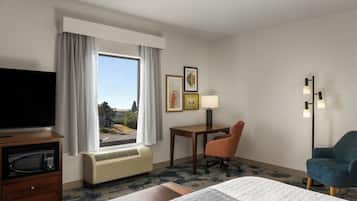 A hotel room with a bed, a desk, a chair, a television, and a window with curtains.