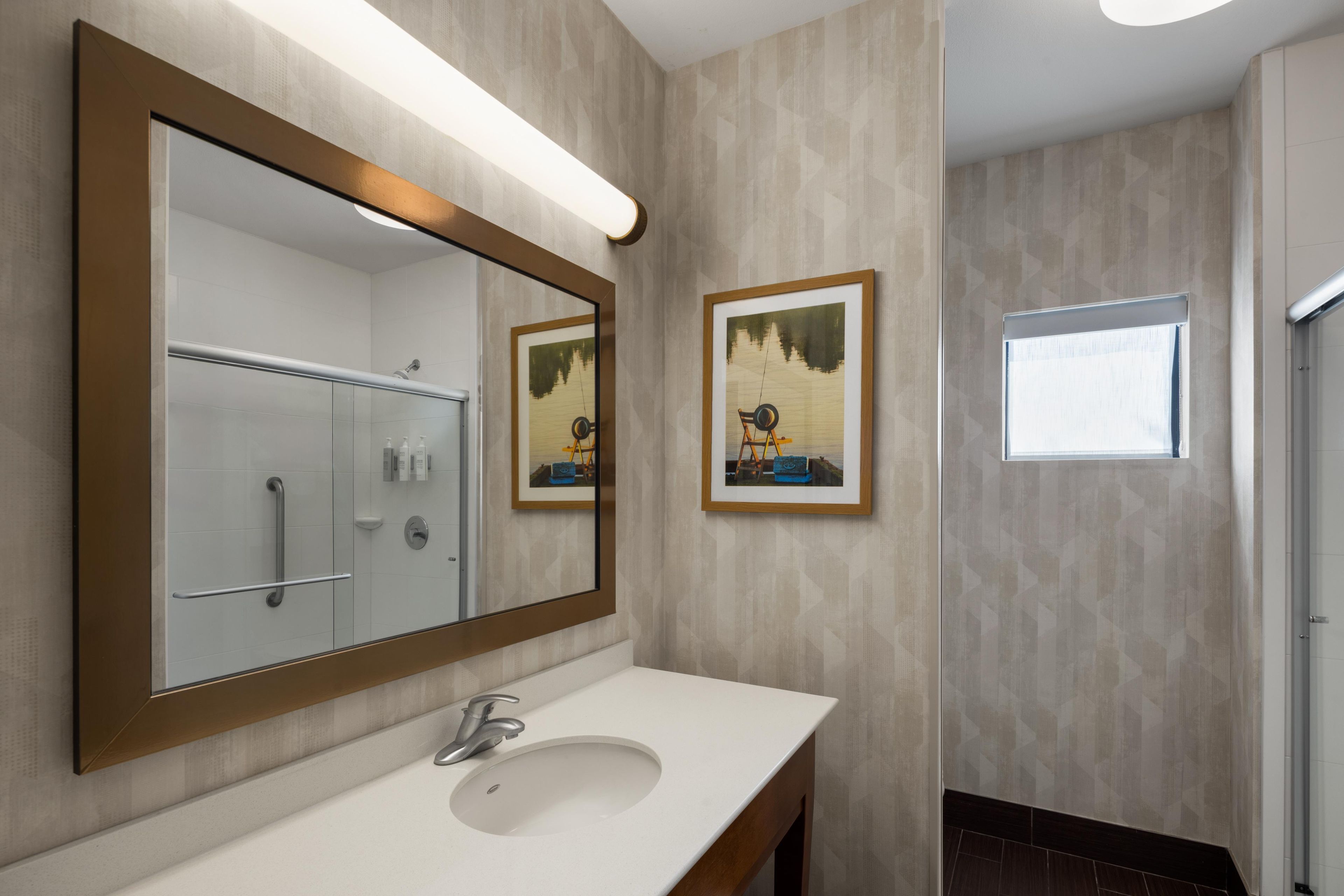 A bathroom with a large mirror, a sink, and two framed pictures on the wall.