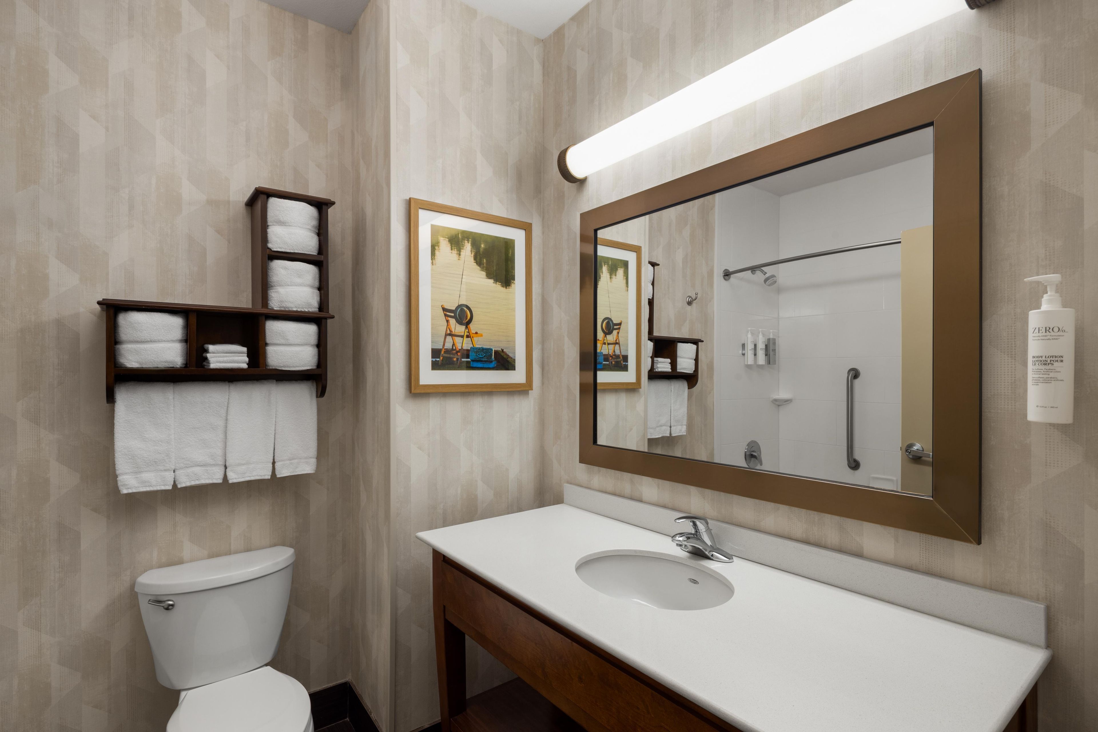 A bathroom with a toilet, a sink, a large mirror, and shelves with towels.