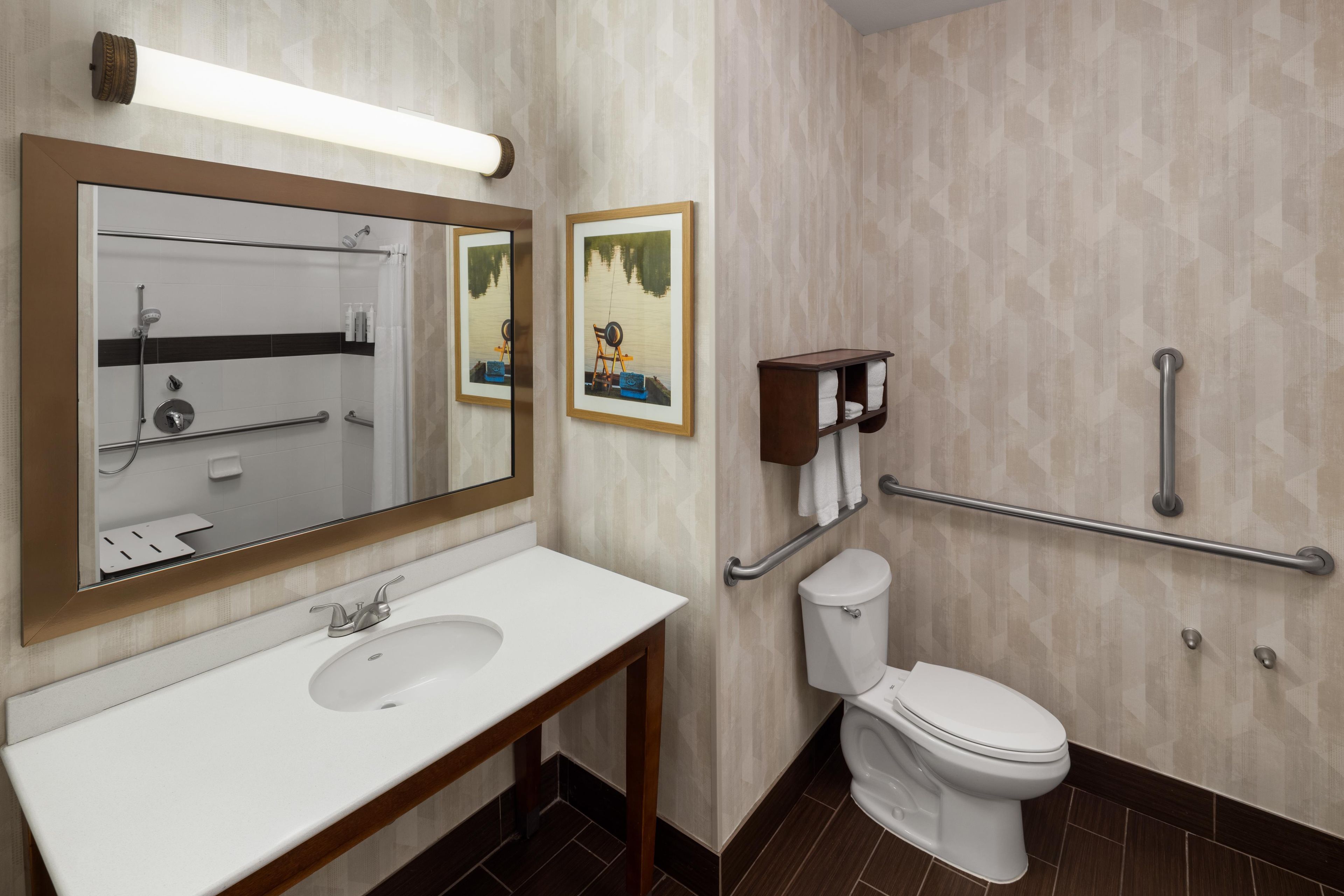 A modern bathroom with a white sink, a toilet, a shower, and two framed pictures on the wall.