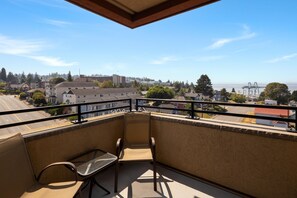 A balcony with a view of a cityscape, a bench, and a railing.