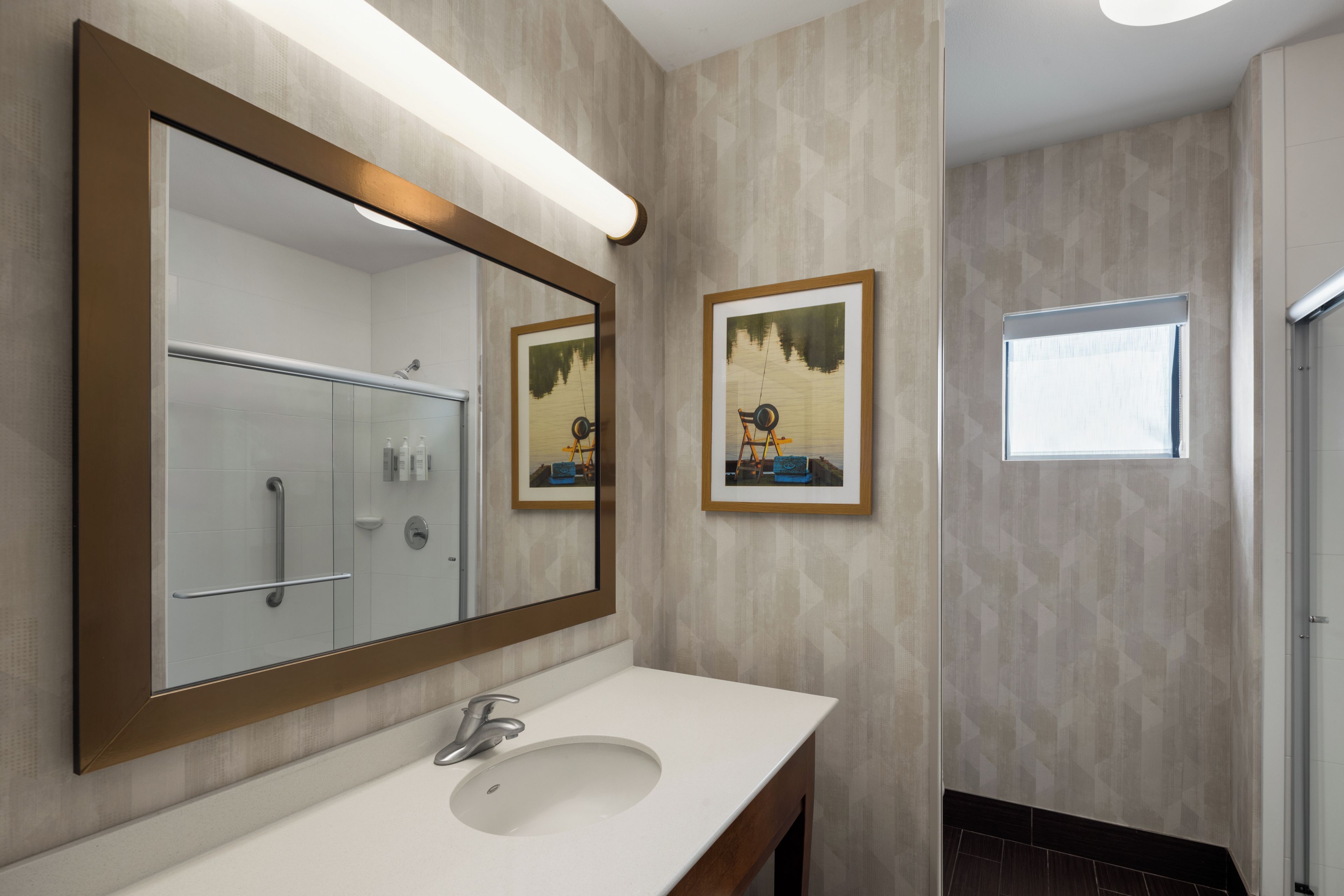 A bathroom with a large mirror, a sink, and two framed pictures on the wall.
