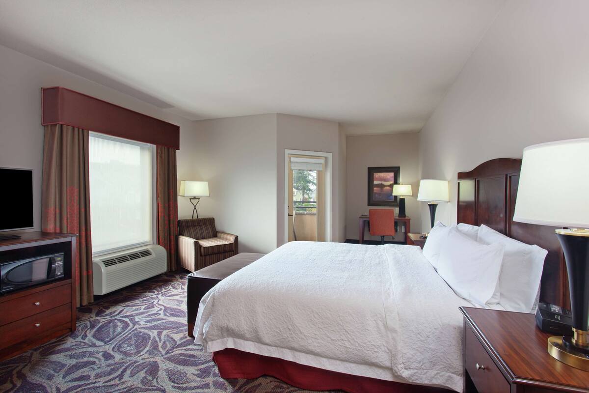 A hotel room with a large bed, a television, a desk, and a window with curtains.