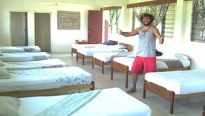 A room with multiple single beds arranged in a row, wooden headboards, and a ceiling fan. - Bamboo Backpackers (Nadi)