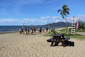 A beach with a picnic table and a sign listing amenities like a beach resort, front office, tour desk, hostel, and free WiFi.