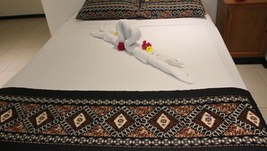 A neatly made bed with a decorative towel and flowers, patterned pillows, and a wooden nightstand with a lamp. - Bamboo Backpackers (Nadi)