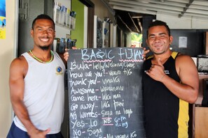 Two individuals holding a sign with basic phrases in a foreign language.