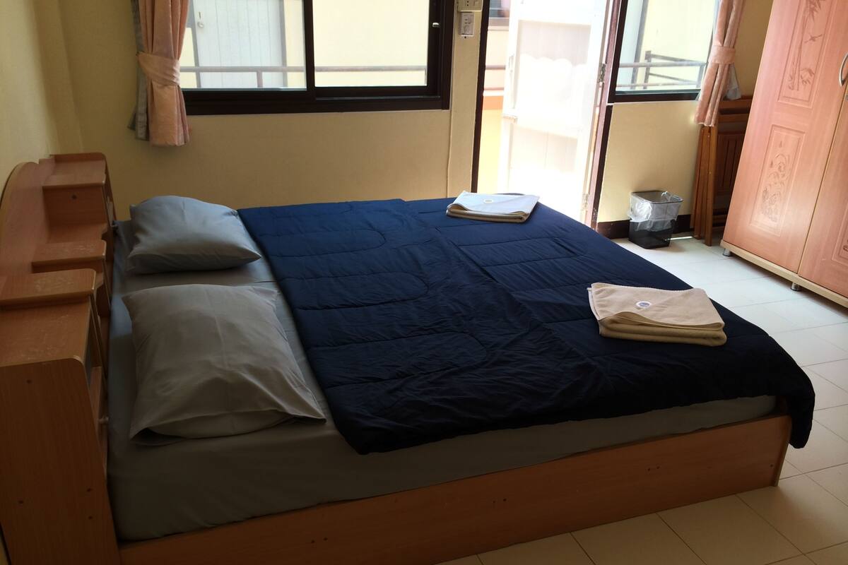 A bedroom with a bed, pillows, a folded towel, a window, and a door.