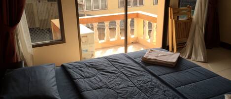 A bedroom with a large bed, a window with a view of a balcony, and a wooden chair.