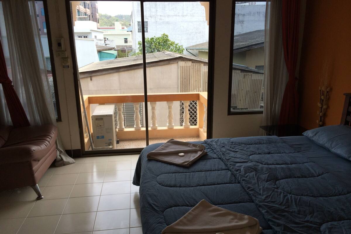 A bedroom with a bed, a chair, and a view through a sliding door to an outdoor balcony.