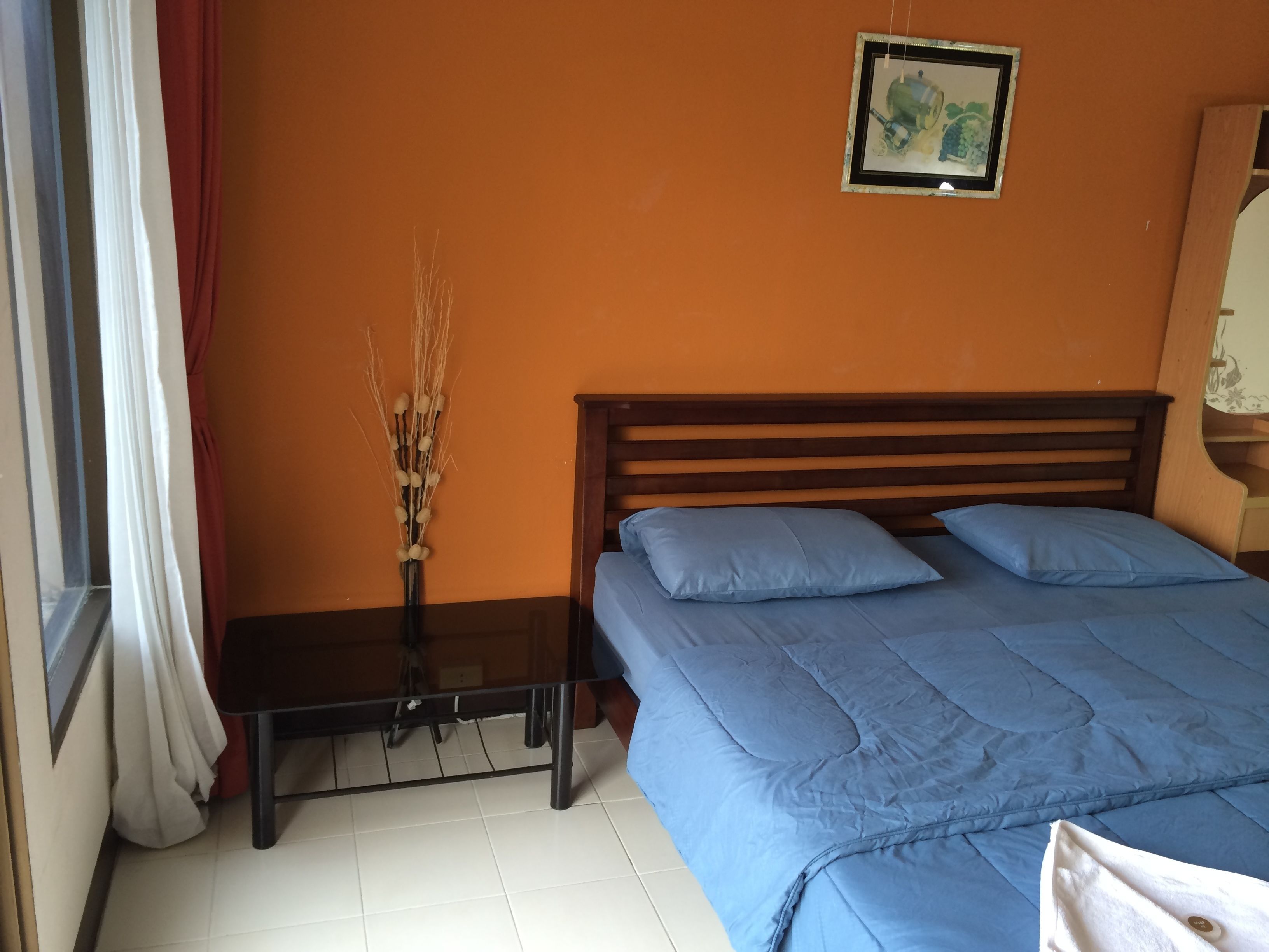 Een slaapkamer met een oranje muur, een houten bedframe en een blauwe sprei.