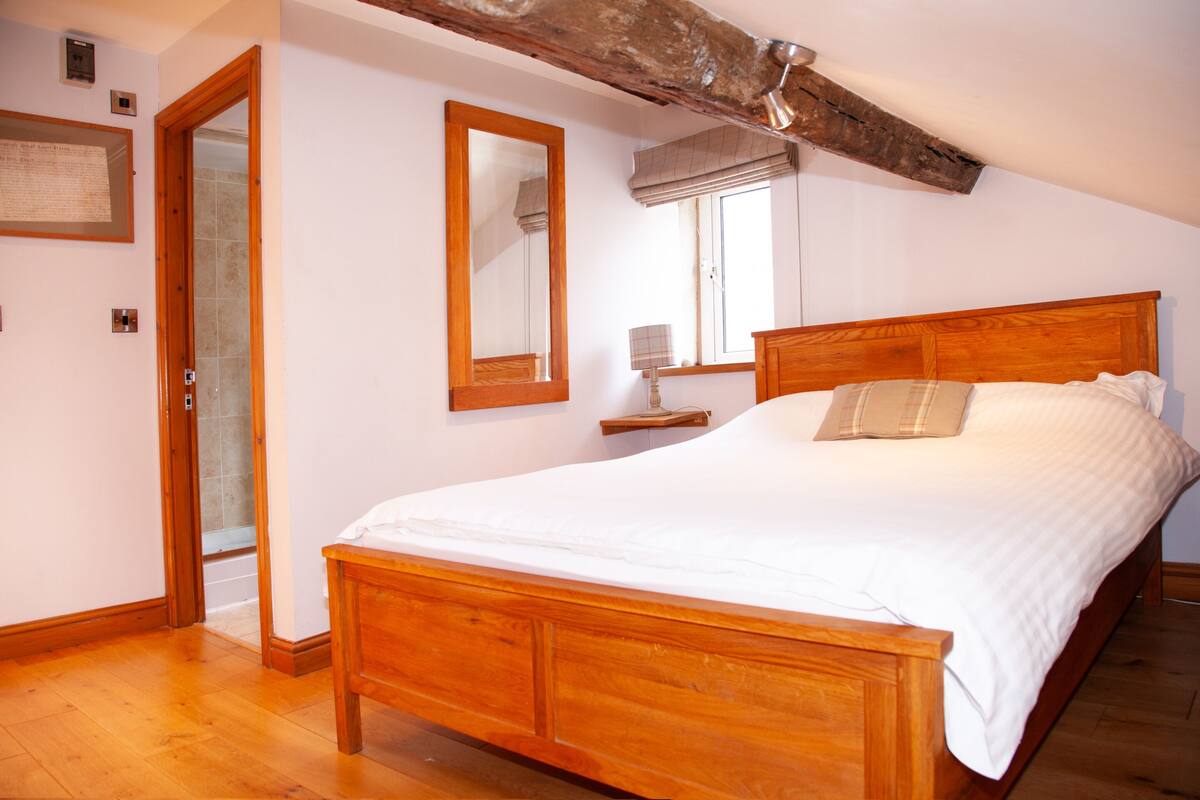 A bedroom with a wooden bed, a large mirror, and a window with a view of the outside.
