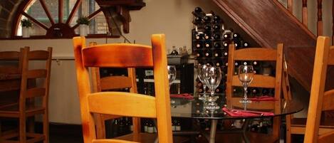 A dining area with wooden chairs and a glass table, a wine rack in the background, and a staircase.