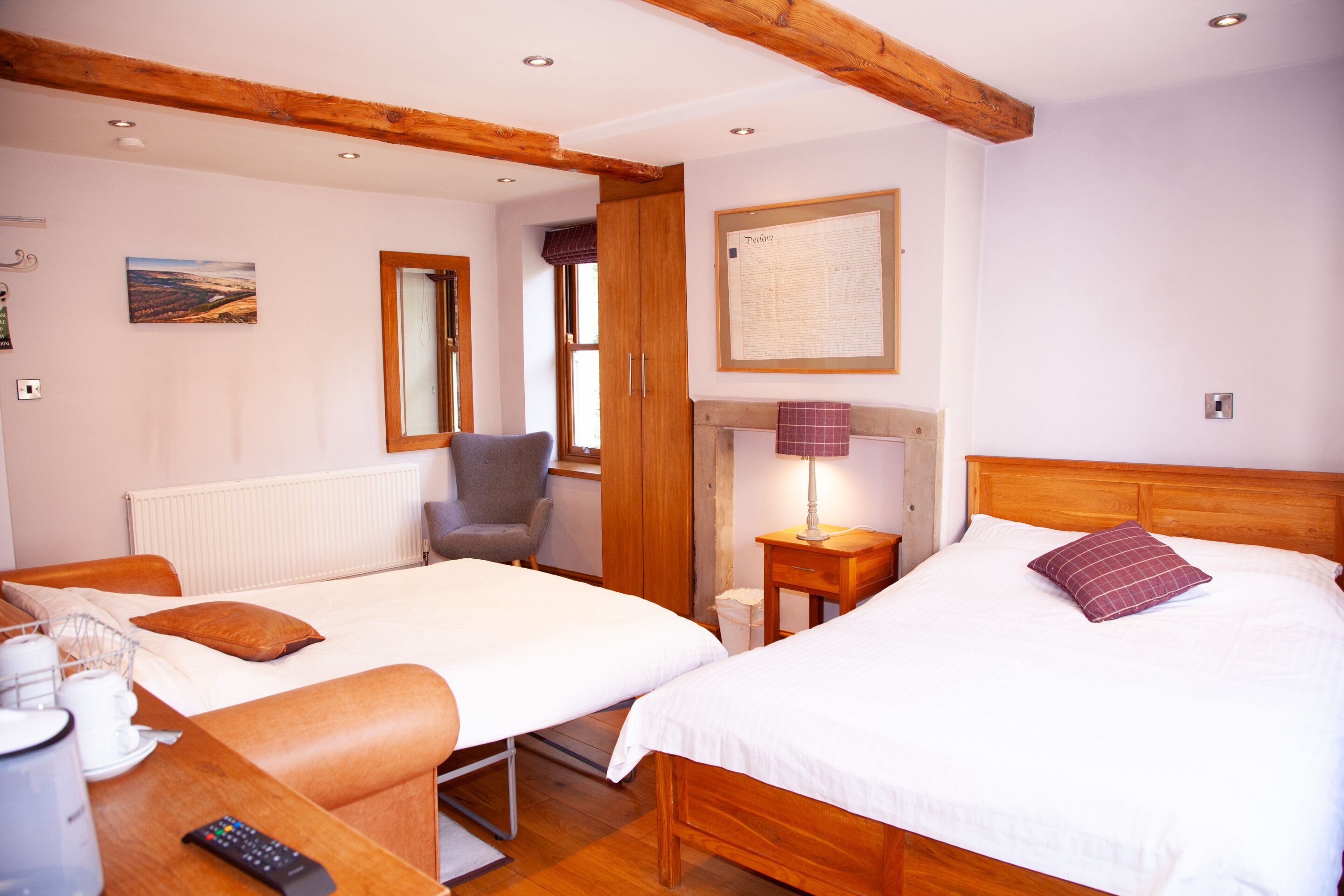 Une chambre d’hôtel avec deux lits, une tête de lit en bois, une chaise, une petite table avec une lampe et un menu encadré accroché au mur.