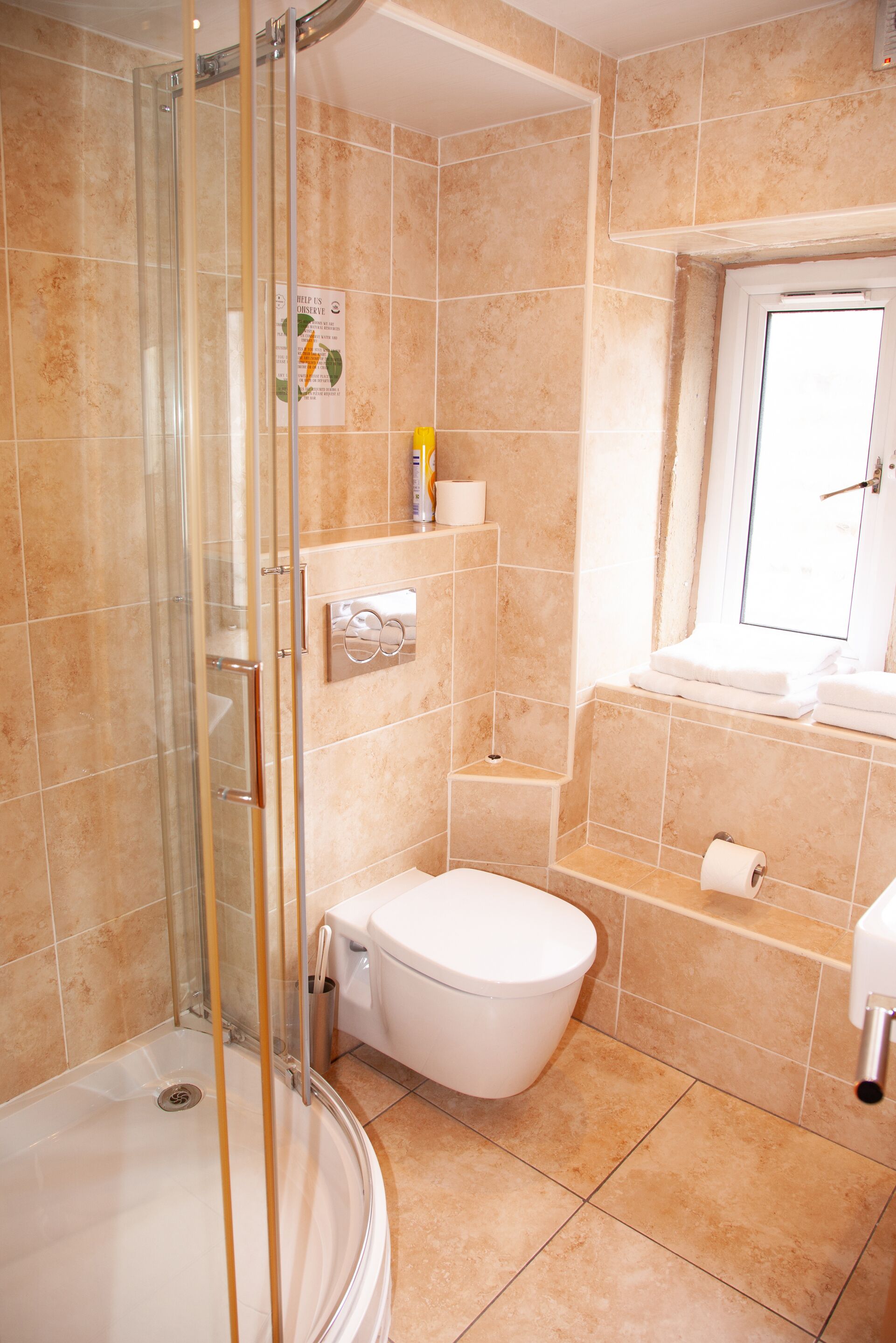 A bathroom with a glass-enclosed shower, a toilet, a sink, and a window.