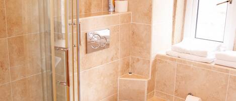 A bathroom with a glass-enclosed shower, a toilet, a sink, and a window.