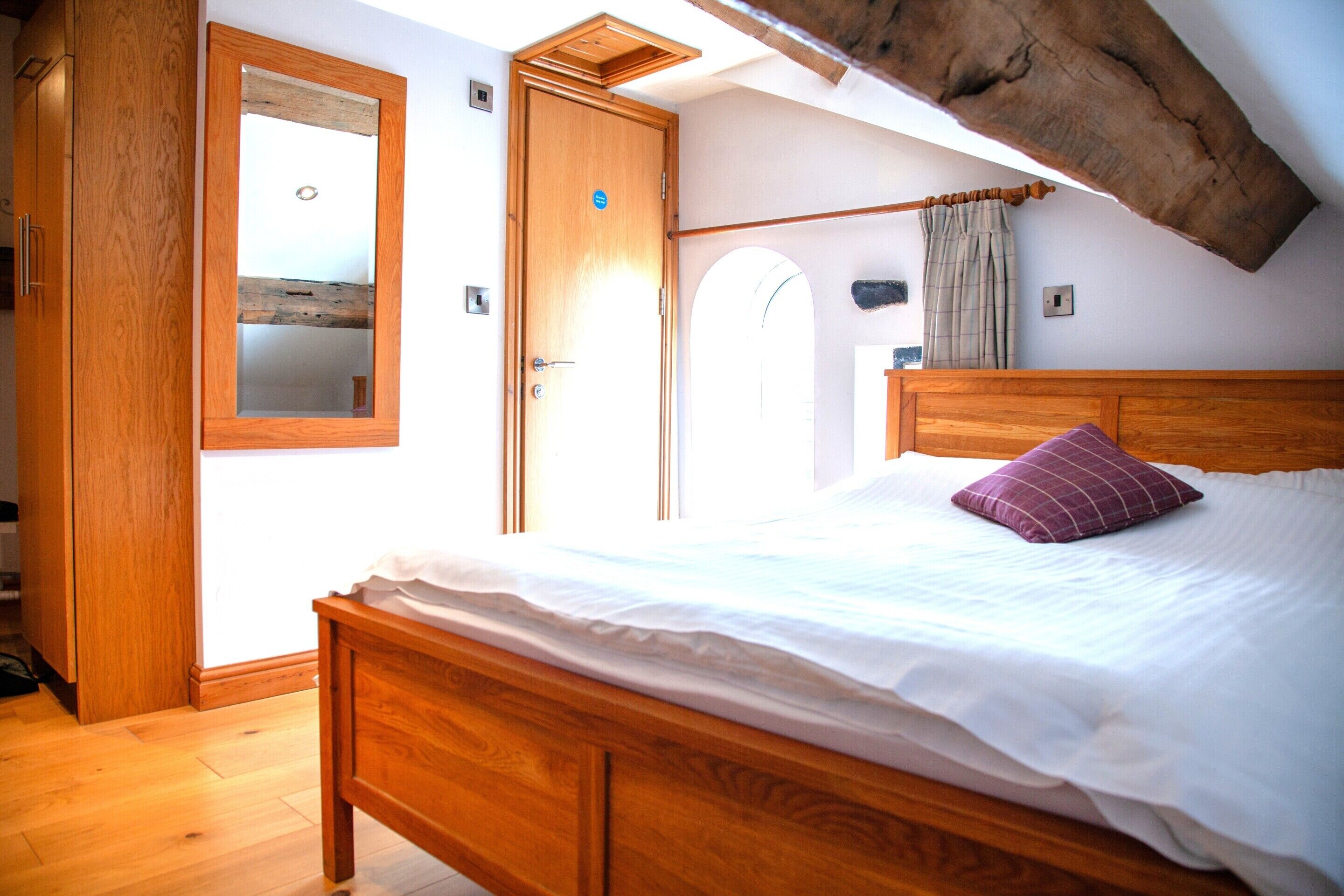 A bedroom with a wooden bed, a large window, and a wooden wardrobe.