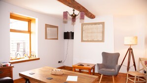Una habitación con una mesa de madera, un sillón gris, un trípode y una lámpara.