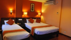 A hotel room with two single beds, each with a pillow and a blanket. There are two bedside tables with lamps, a wall-mounted air conditioner, and a painting above the beds. - Rama Inn Boutique Home (Kathmandu)