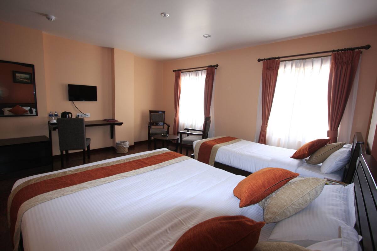 Quarto de hotel com duas camas, uma escrivaninha, uma cadeira, uma televisão e uma janela com cortinas.