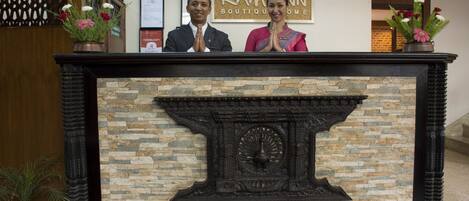 A reception desk with a stone and wood design, a framed welcome sign, and potted plants.